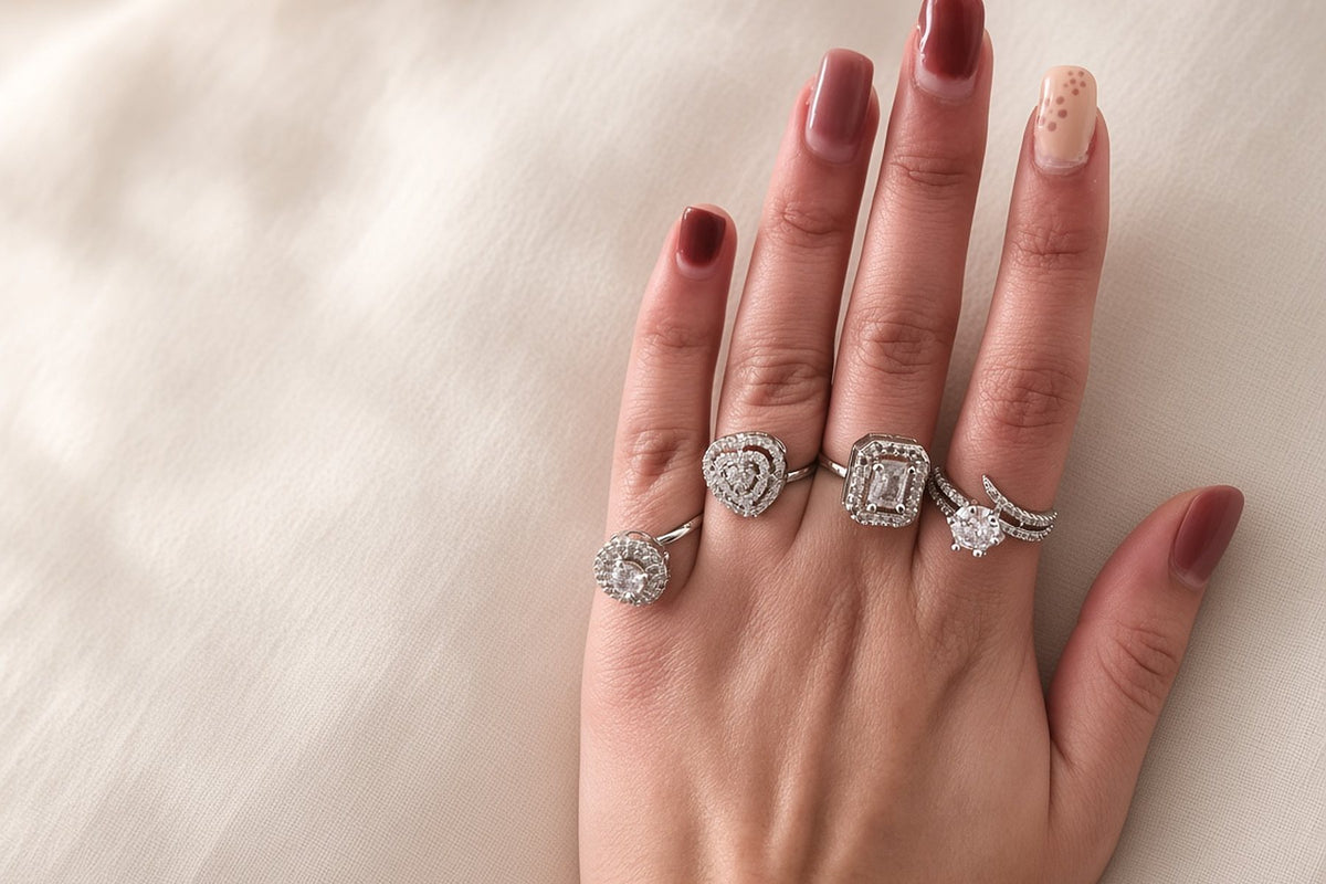 Four silver cubic zirconia cocktail rings stacked on a hand: halo solitaire, heart halo, emerald-cut halo and crossover solitaire