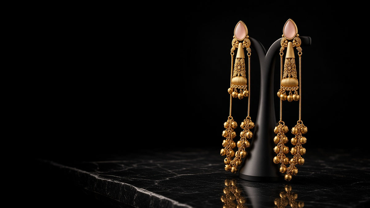 Gold ghungroo jhumka drop earrings with pink stones on a black stand against a dark background